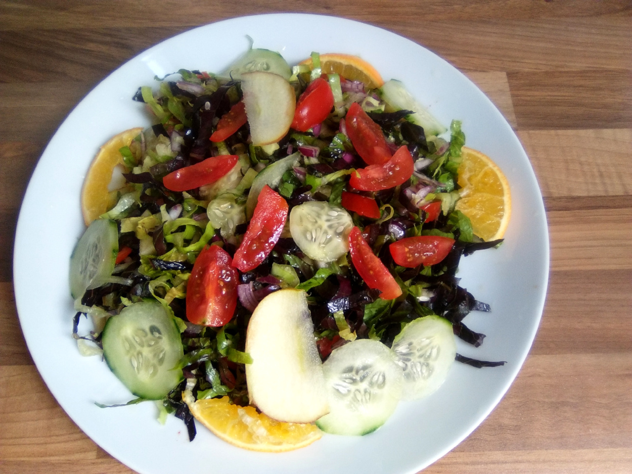 Healthy salad decorated with cucumber, orange wedges, and tomatoes